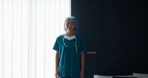 Asian nurse in a bedroom showing the difference between daylight and Ministry of Blind blackout roller blinds for shift workers